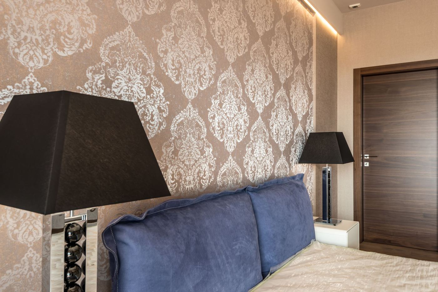 Luxurious bedroom with champagne and ivory damask wallpaper, a blue velvet headboard and black lamps