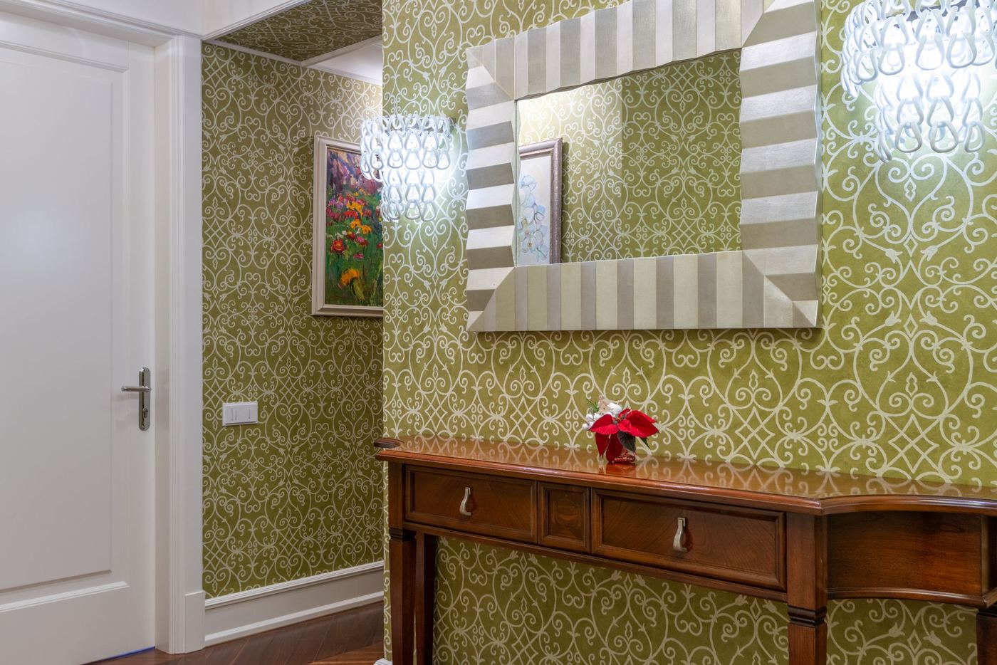 Hallway with olive-green ornamental wallpaper, a silver-framed mirror and a wooden console table